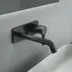 Wand-Waschtischarmatur von Ideal Standard in mattem Schwarz, mit eckiger Rosette und langem Auslauf, montiert an heller Wand über einem weißen Waschbecken.